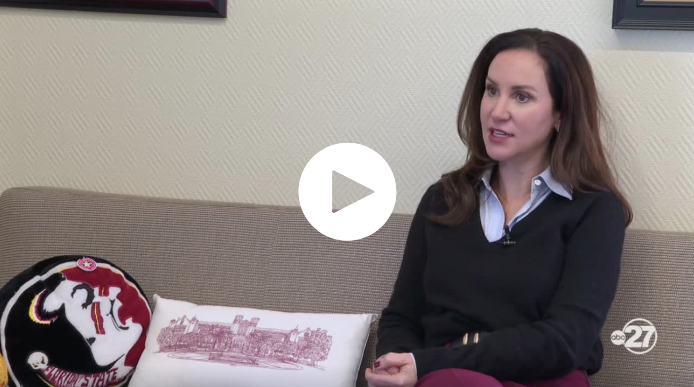 FSU DSA VP Dr. Amy Hecht speaks about food insecurity sitting on a gray couch with fsu memorabilia