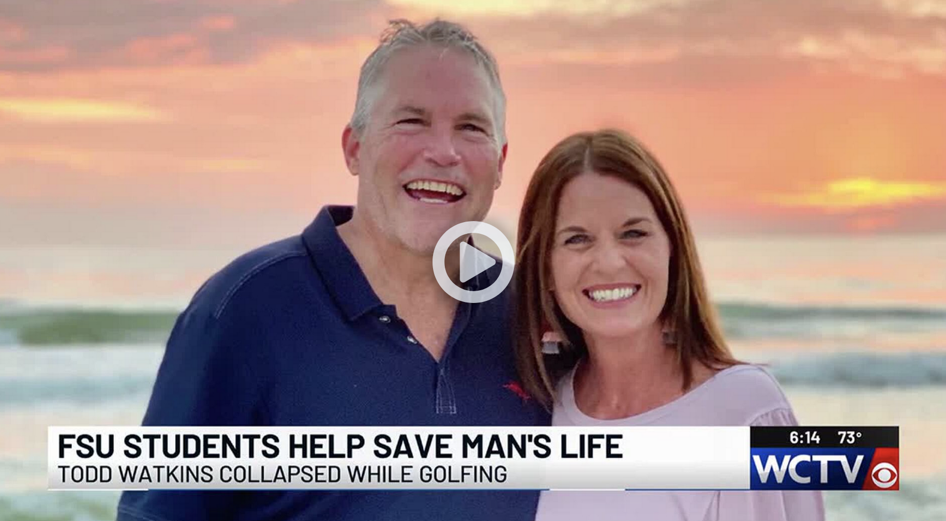 still picture of Todd Watkins and his wife posing in front of asunset. There is a play button superimposed over their faces.