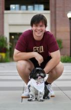 student smiling holding his dog wearing an FSU bandana