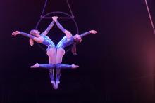two women dressed in blue leotards hanging from a hoop