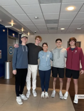 four male students standing shoulder-to-shoulder with smiling woman